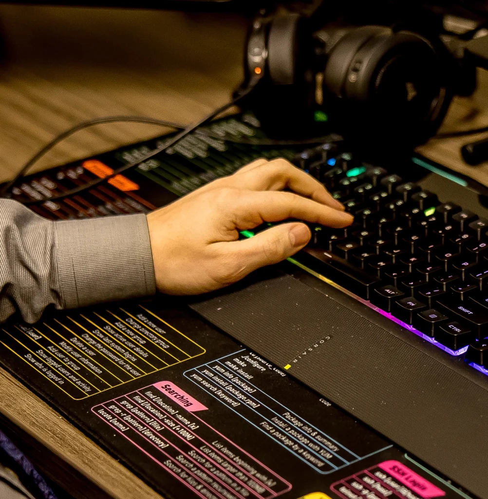 A mans hand typing on a RGB keyboard with headphones charging on the desk