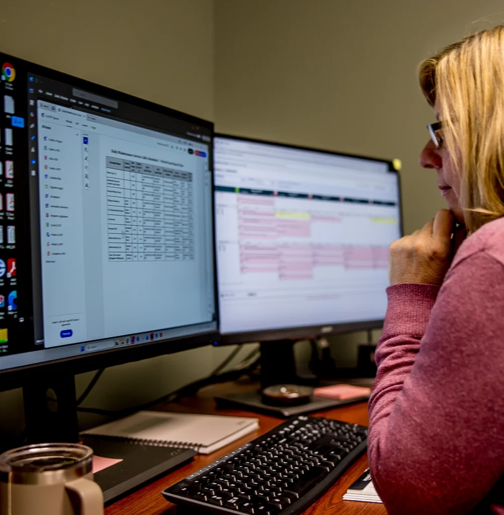 Woman in pink looking at a monitor with spreadsheets