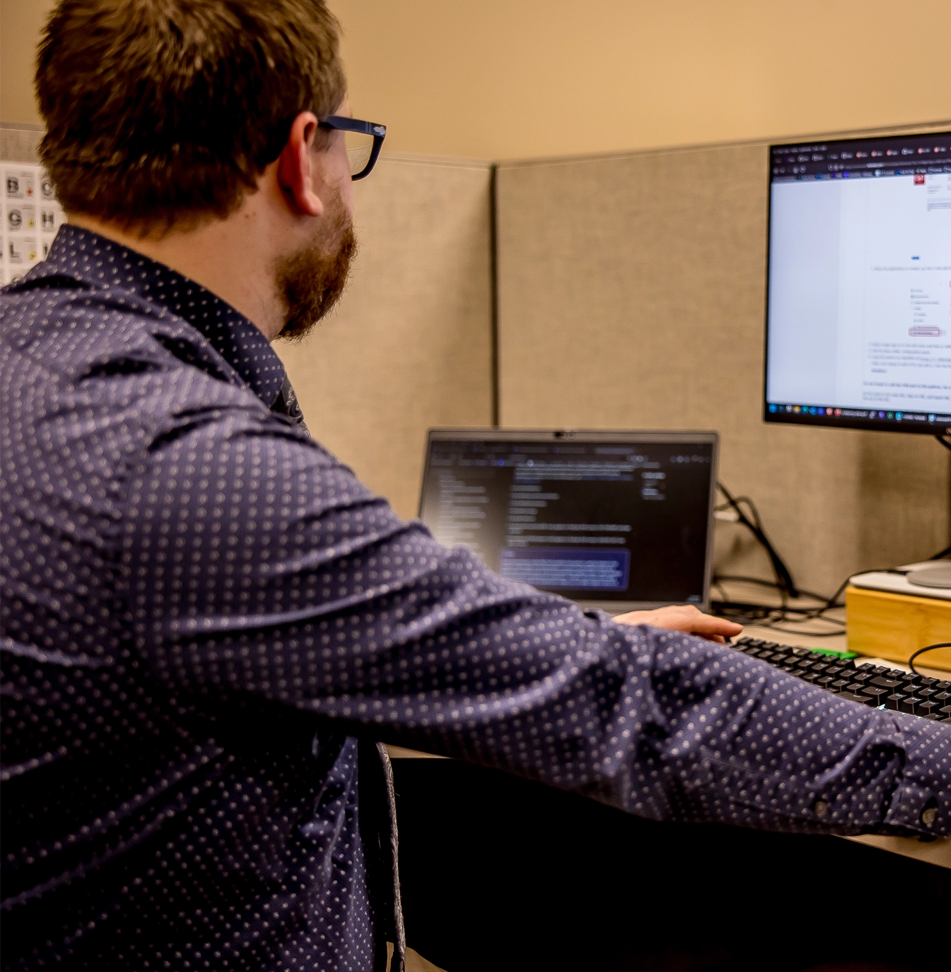 Man working at a desk with a laptop and external monitor